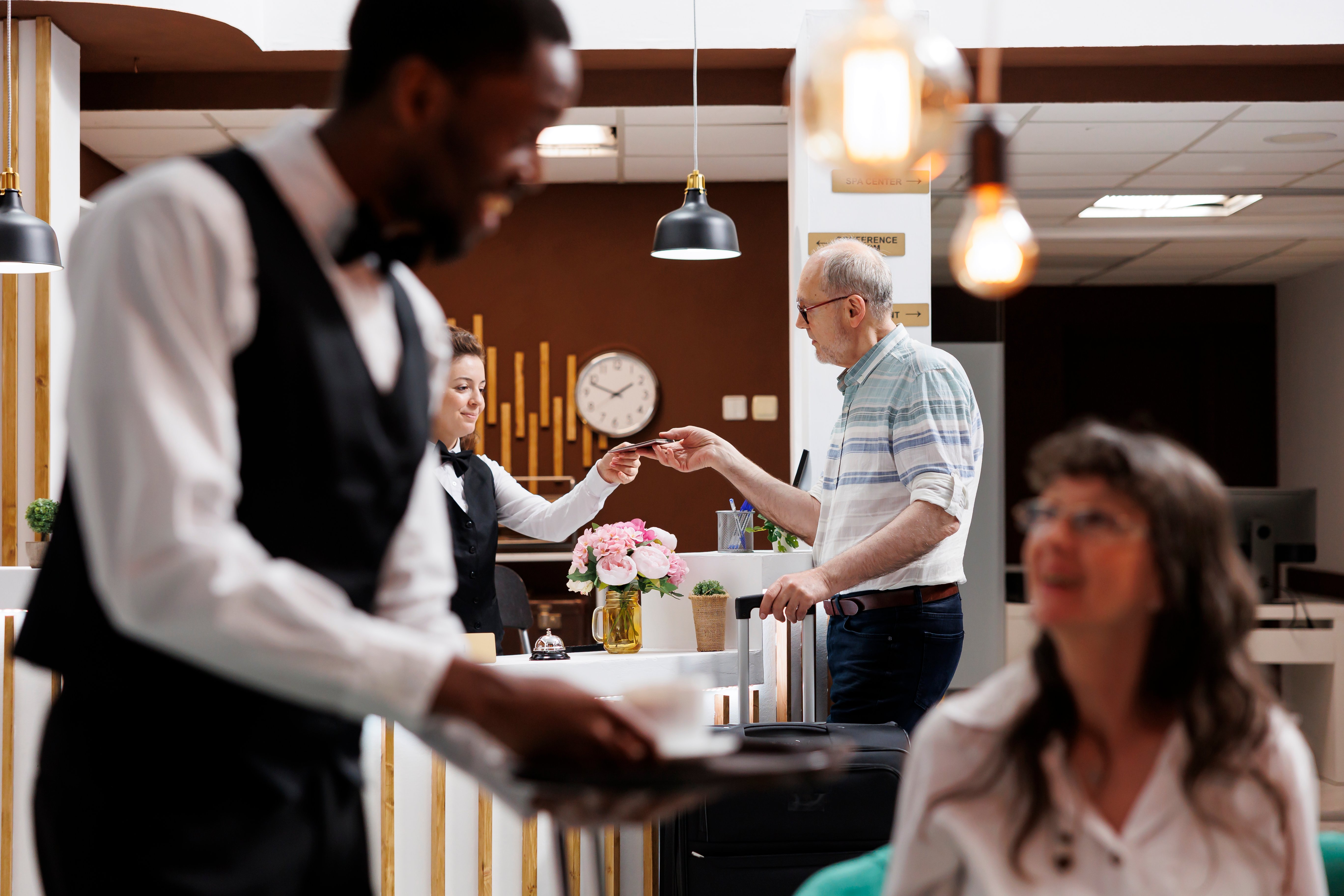 caucasian-receptionist-helps-retired-old-man-with-hotel-checkin-verifying-identity-retrieving-reservation-details-female-concierge-holds-checks-passport-male-tourist-focus-background